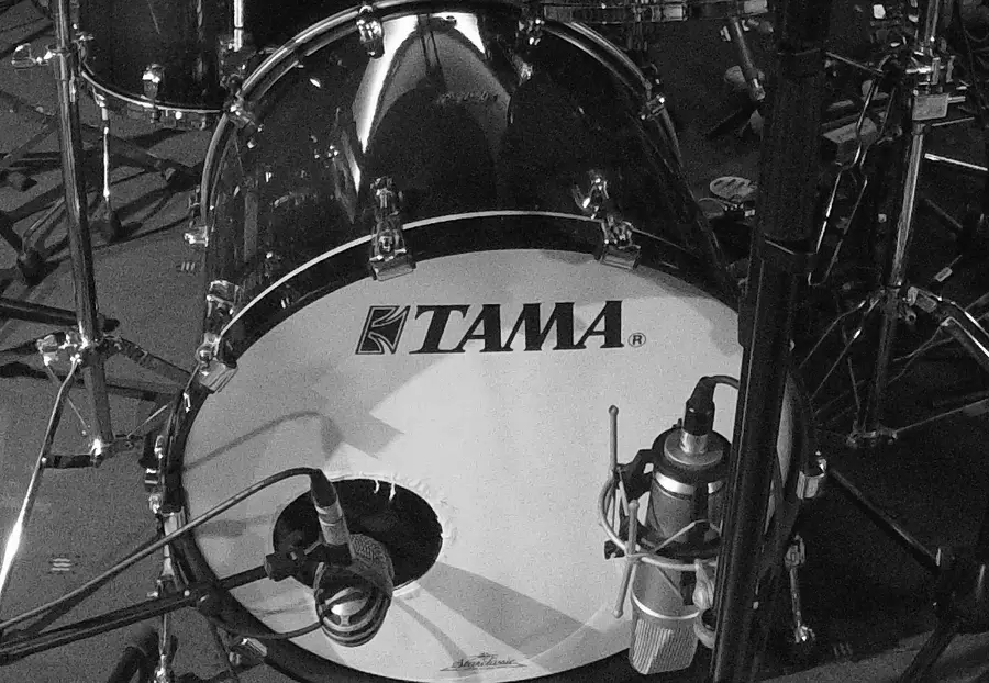 Black-and-white photograph of a bass drum set up with two microphones: a dynamic microphone inside the port hole and a condenser microphone in front of the head.