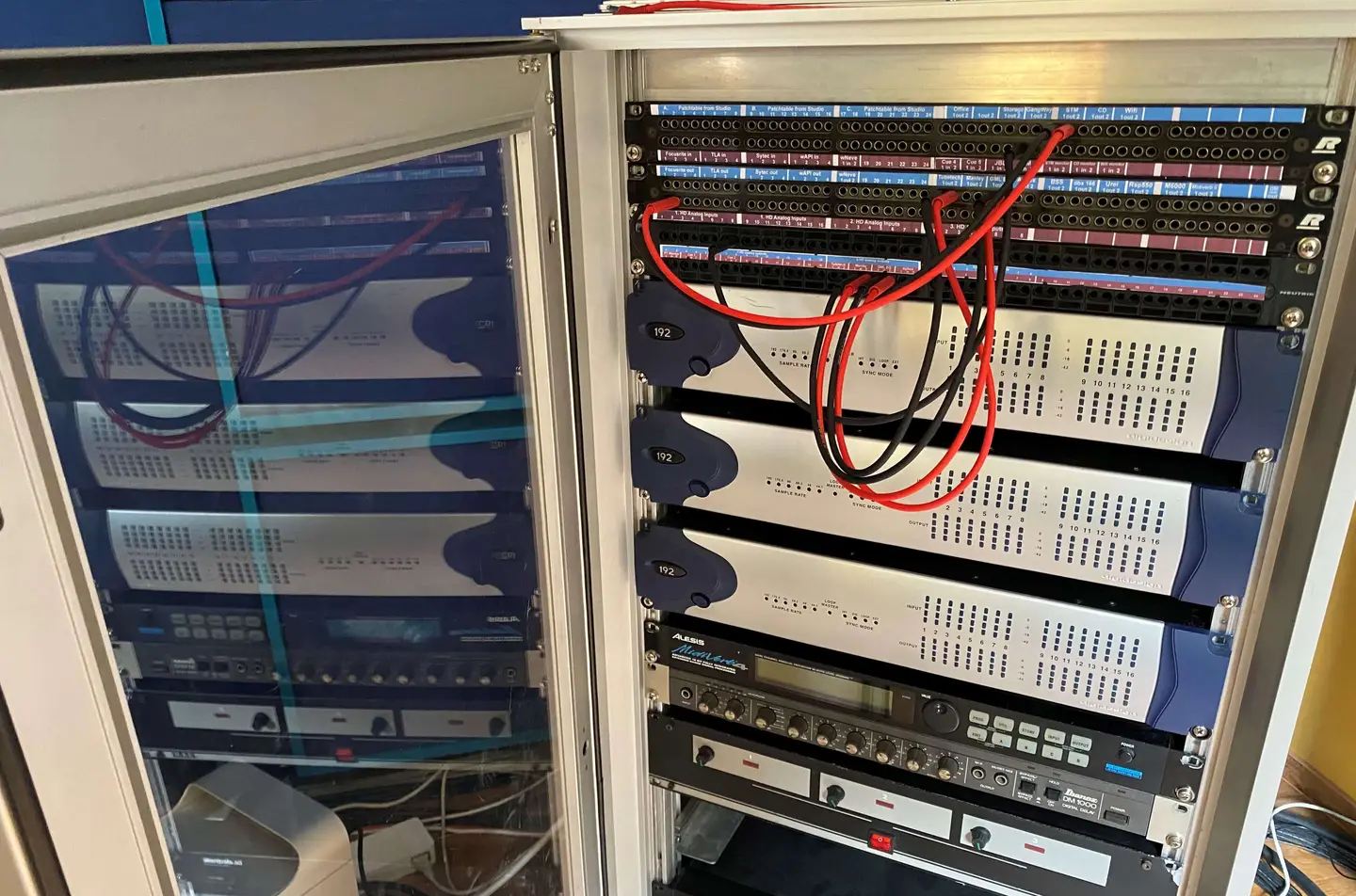 Open nineteen-inch rack with labelled patchbays and three Avid 192 I/O audio interfaces, patch cables connected across the top row.
